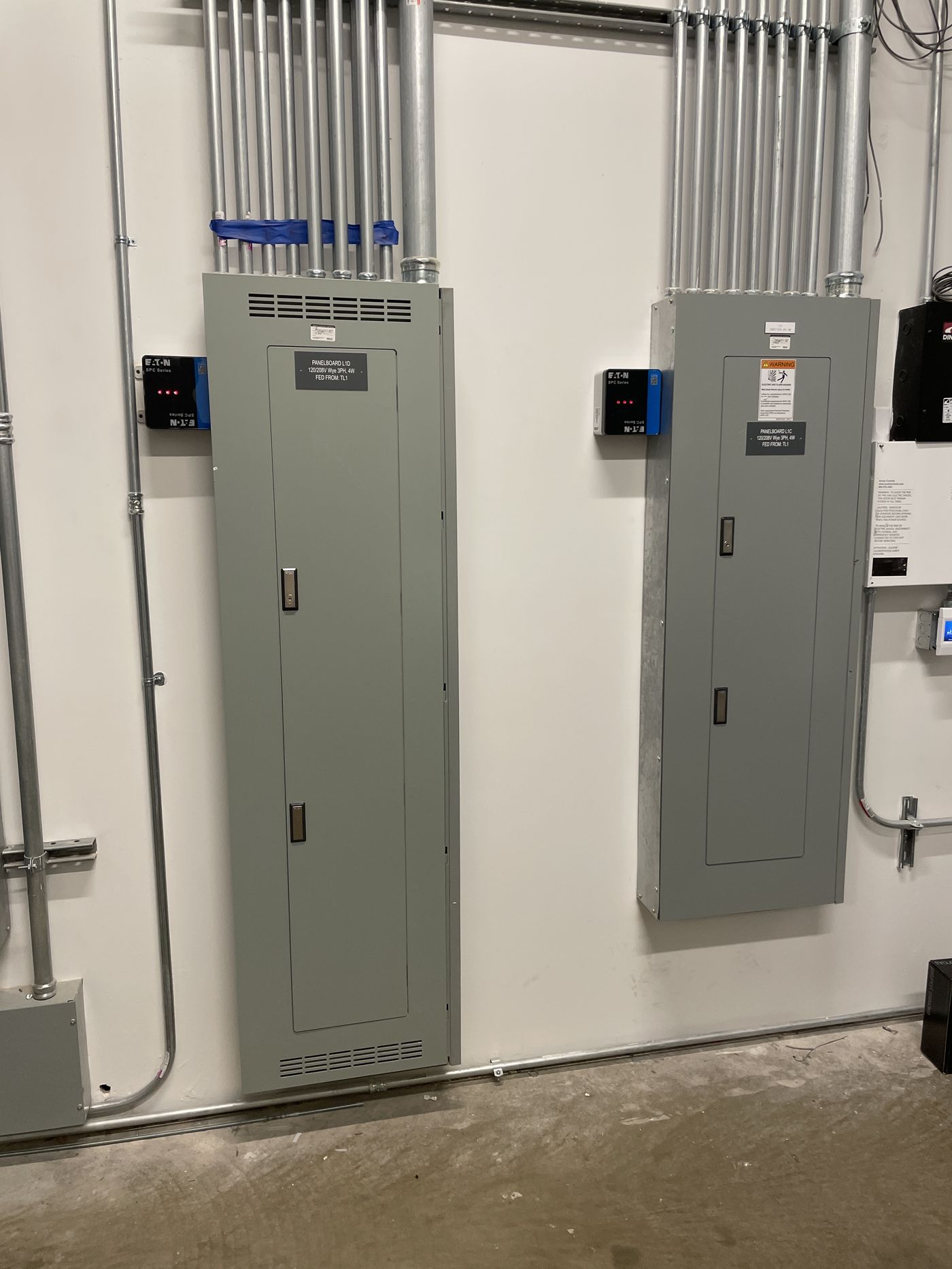 Two commercial panelboards with labeled surge protection and neat conduit runs in an electrical room