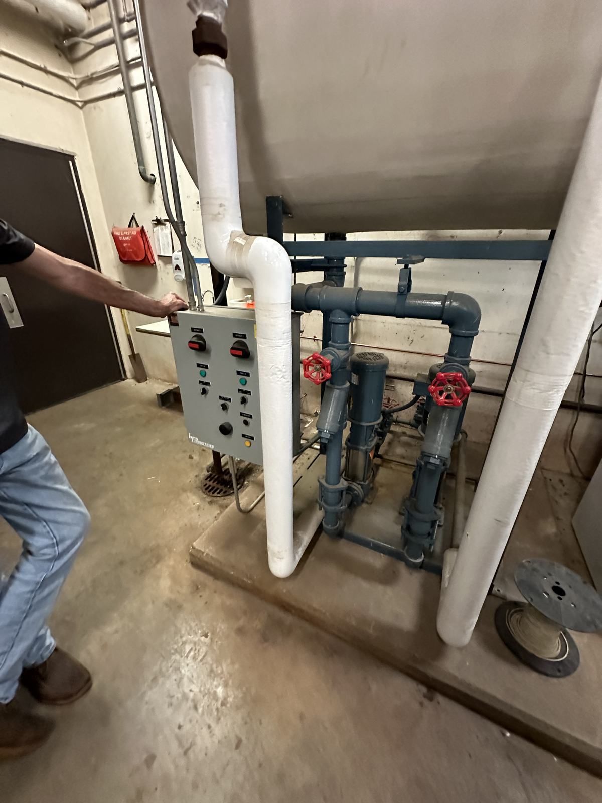 Electrician at a duplex pump control panel in a commercial mechanical room