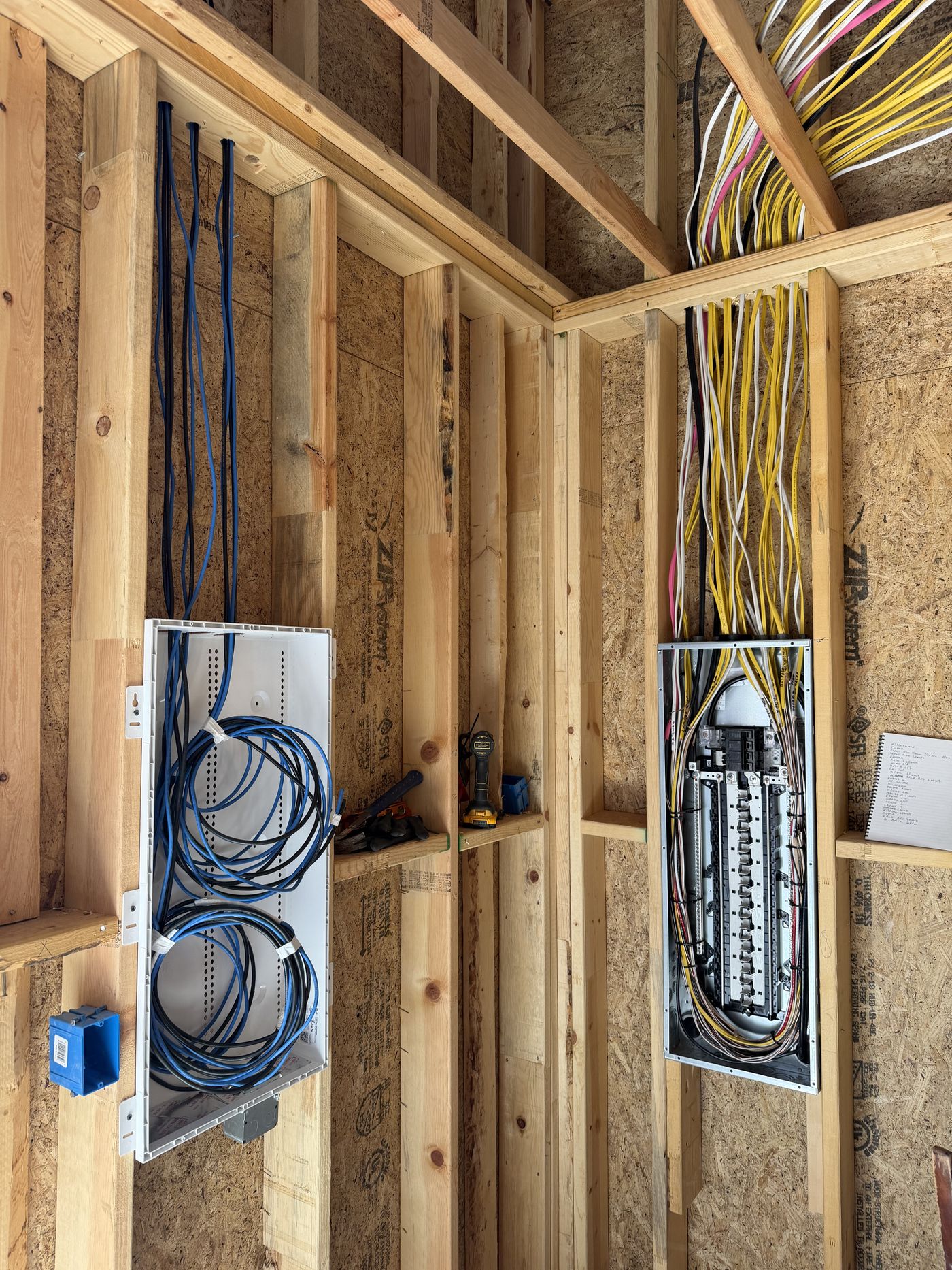New construction electrical rough-in with a breaker panel and low-voltage panel wired in open framing