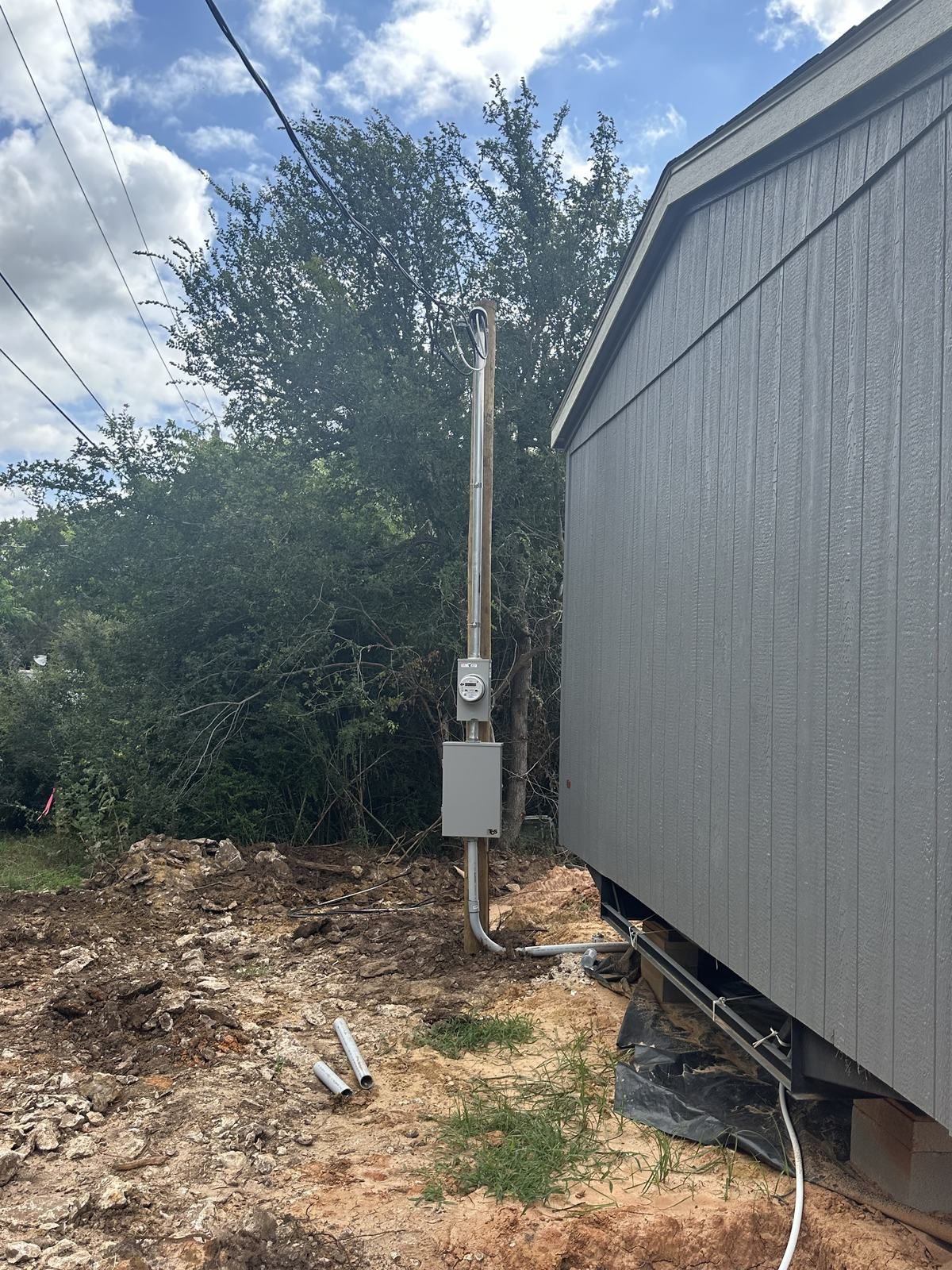 New residential electrical service pole with meter and disconnect installed beside a gray Texas home