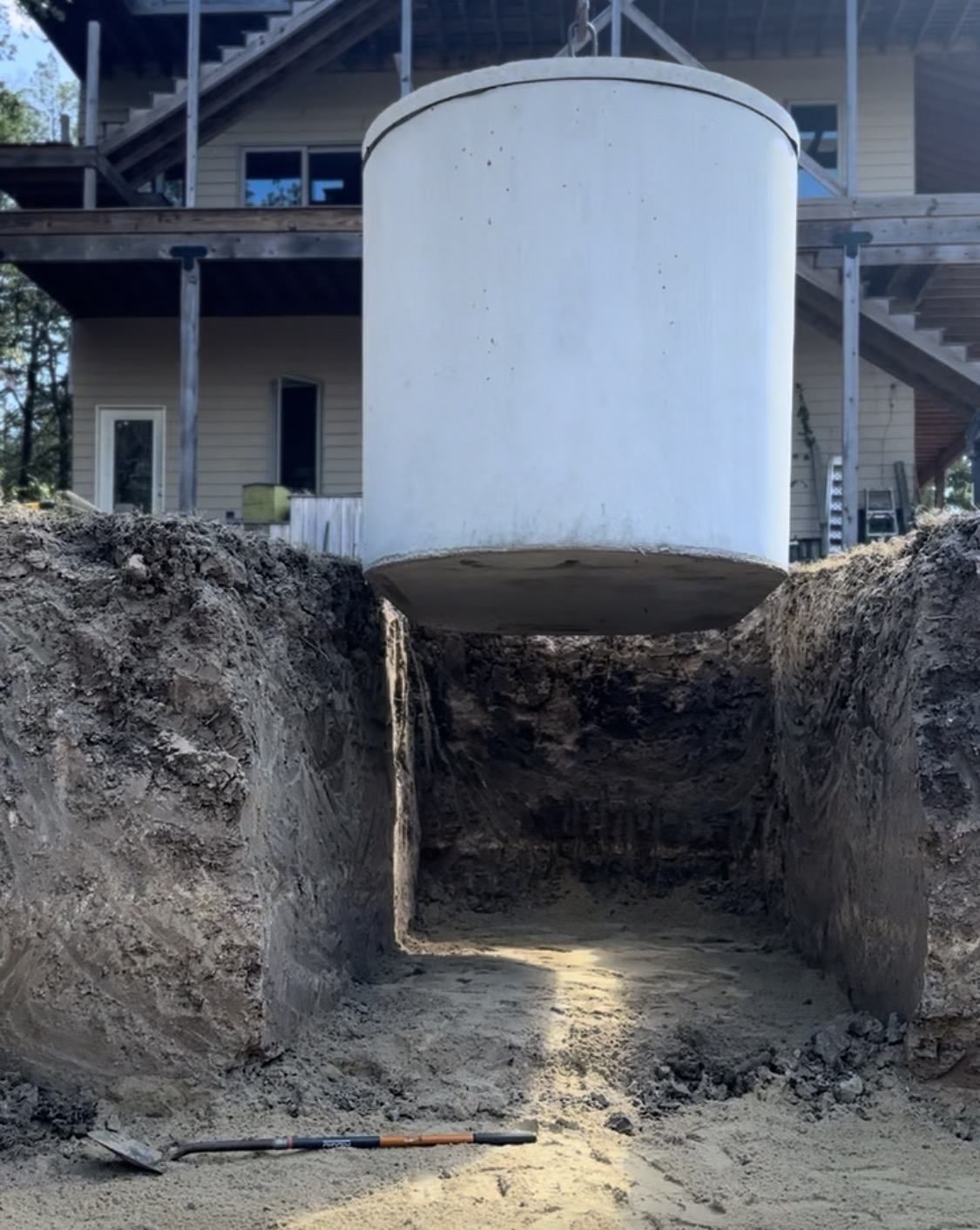 Concrete septic tank being lowered by crane into a freshly excavated pit in front of a Texas home